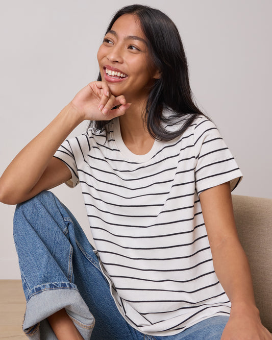 Model wearing Classic Cotton Nursing T-shirt in White & Black Stripe sitting on a lounging chair in a relaxed pose laughing