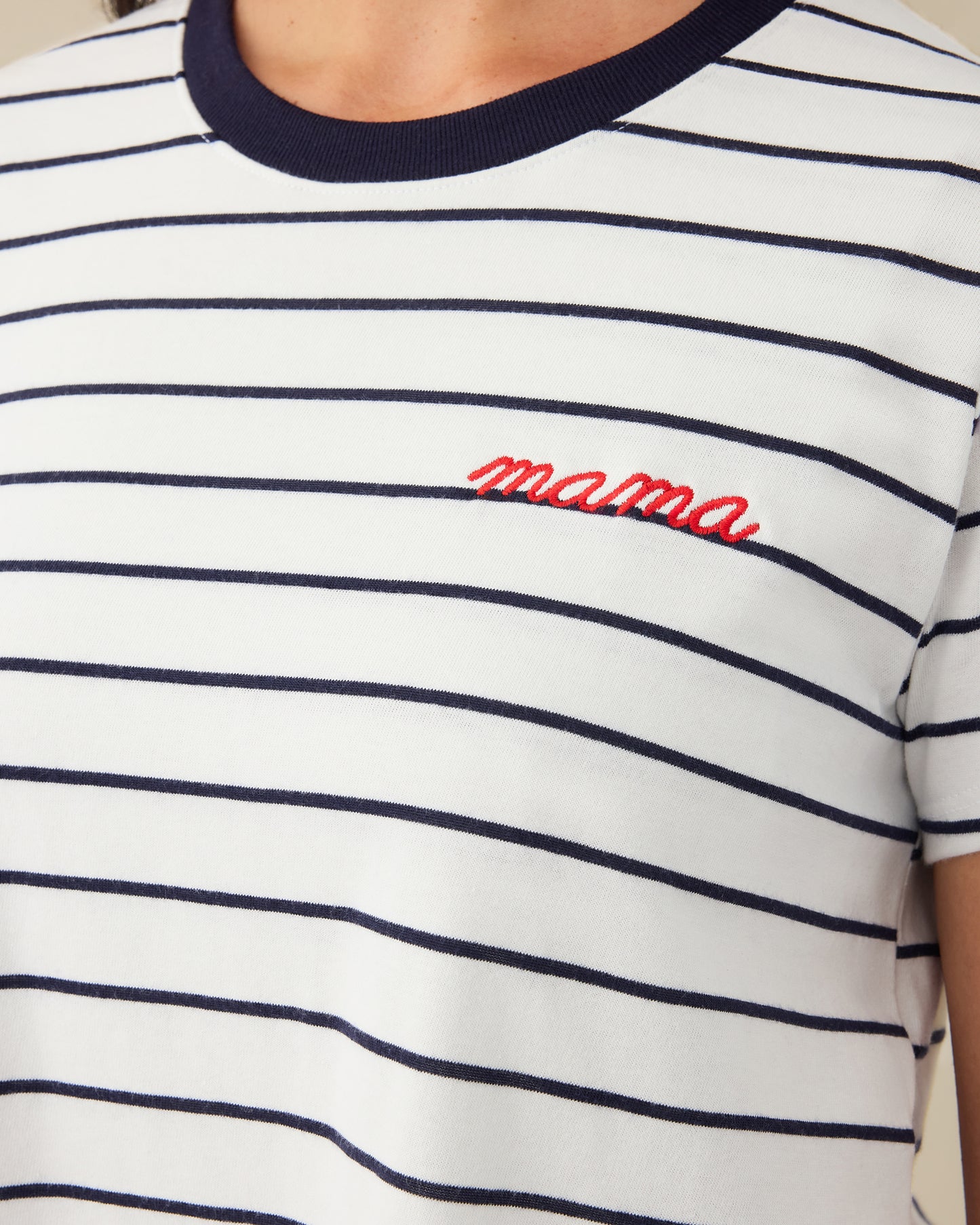 Close up of Classic Cotton Nursing T-shirt in Navy & White Stripe - Embroidered, with the red-threaded word, mama, on a beige background.