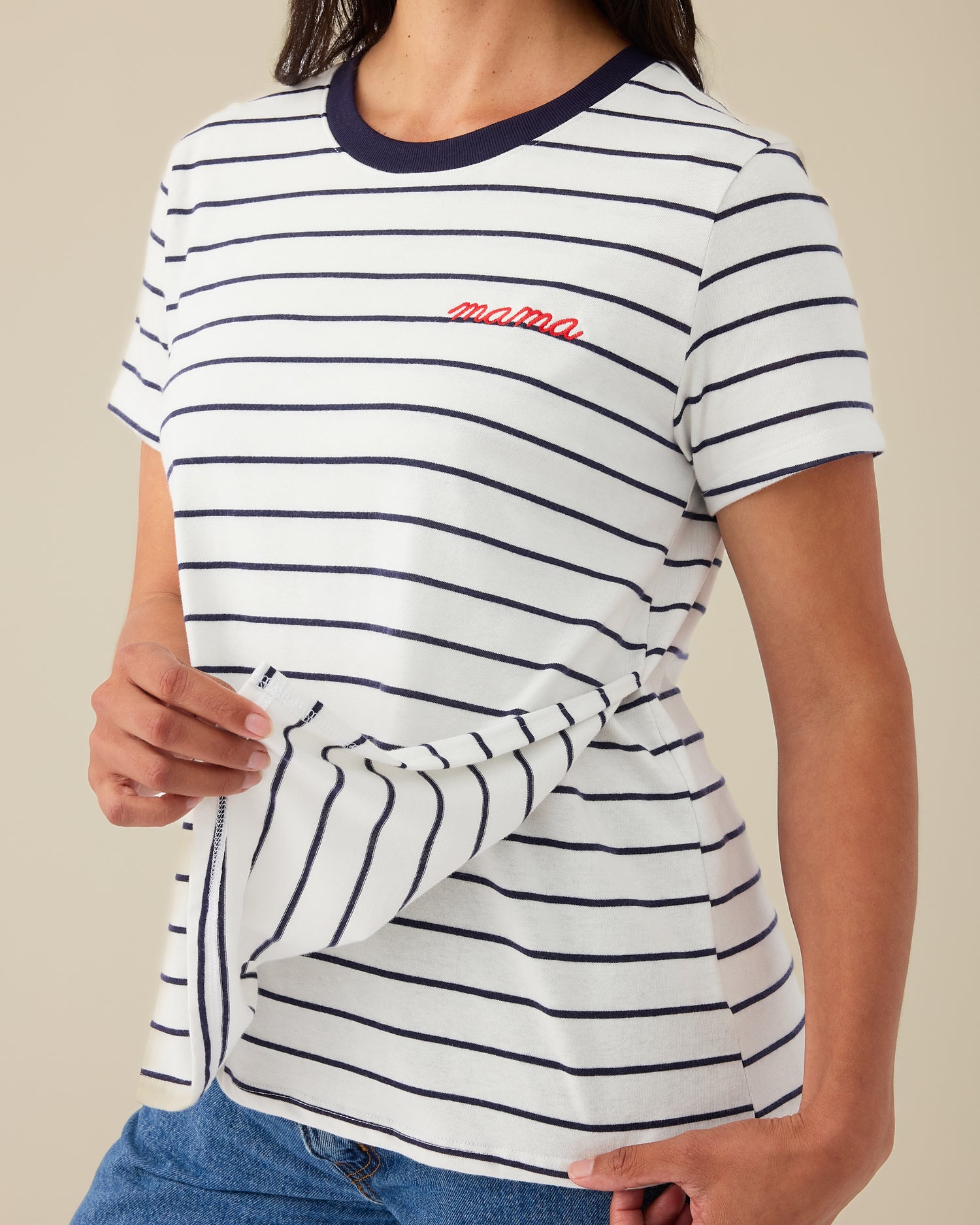 Model is flipping up the front panel of the Classic Cotton Nursing T-shirt in Navy & White Stripe - Embroidered, with the red-threaded word, mama, on a beige background.