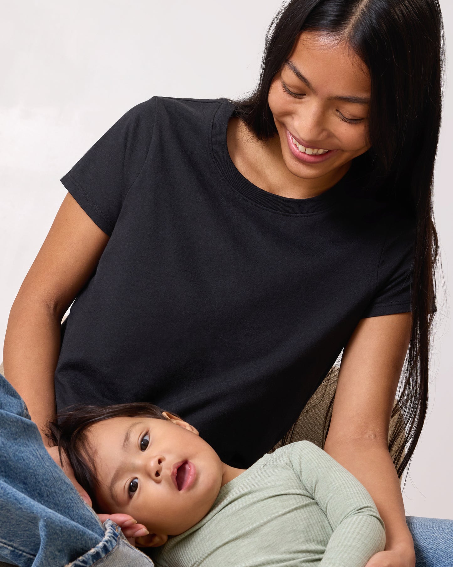 Model wearing Slim Fit Cotton Nursing T-shirt in Black sitting on the floor smiling at the baby lying on her lap