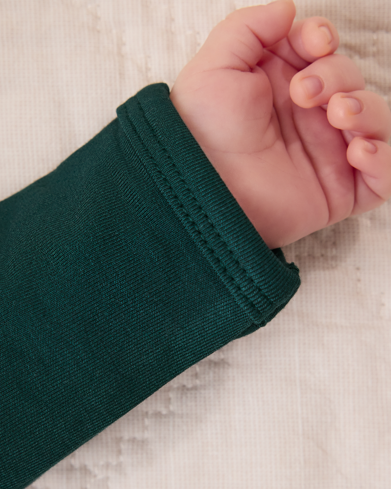 Close-up of a baby's hand wearing Close-up of baby wearing the Cozy Bamboo Baby Gown & Hat in Evergreen on a light background