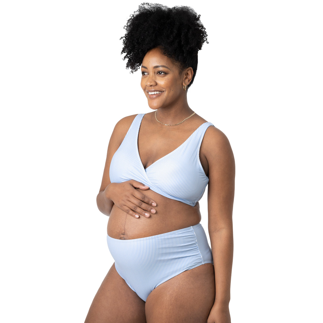 Pregnant model wearing the Crossover Maternity & Nursing Bikini Top with her hand on her belly. @model_info:Roxanne is wearing a Large.