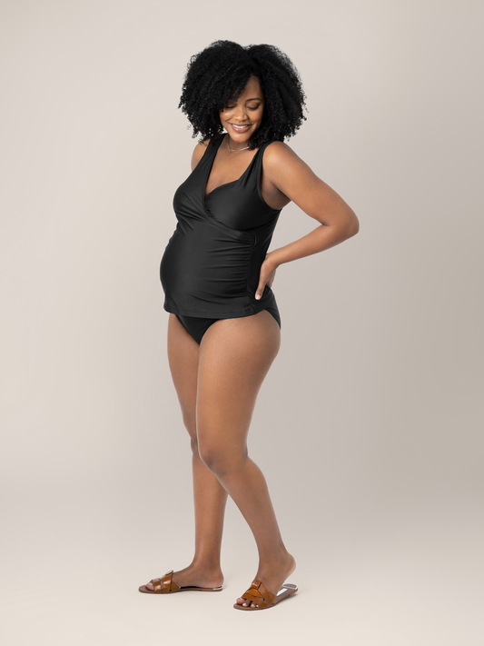 Pregnant model wearing the Crossover Maternity & Nursing Tankini in Black with her hands on her hips. @model_info:Roxanne is wearing a Large.