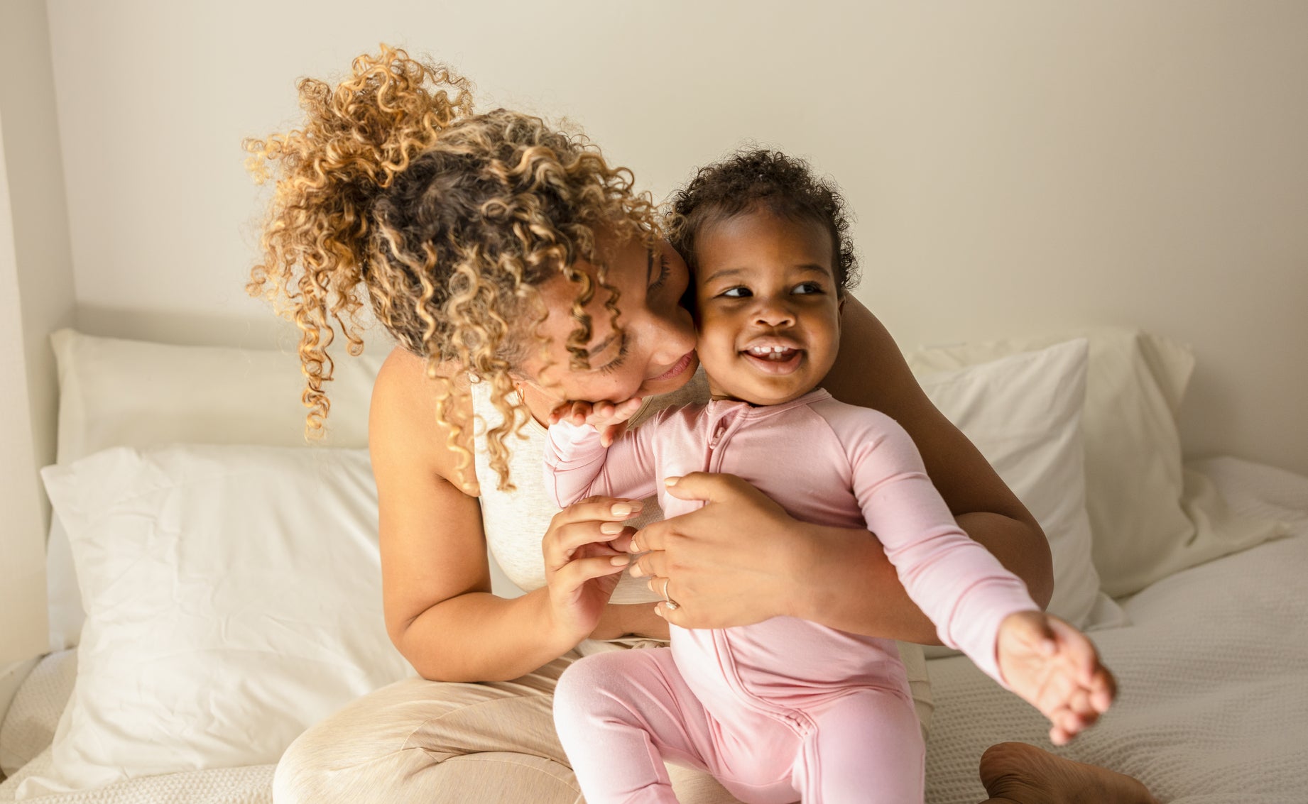 Baby wearing the Bamboo Baby Pajamas in Light Mauve while sitting on a bed with her mom, smiling.
