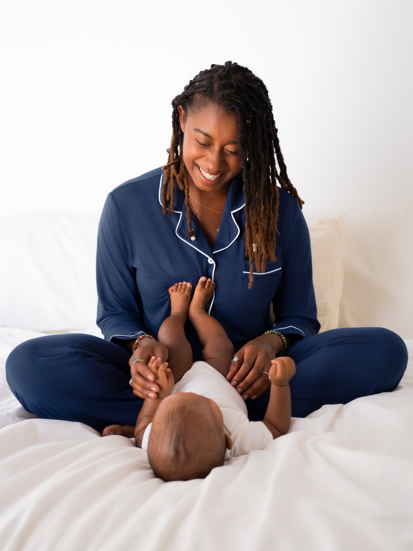 Model sitting on bed playing with baby and wearing the Clea Bamboo Long Sleeve Pajama Set in Navy