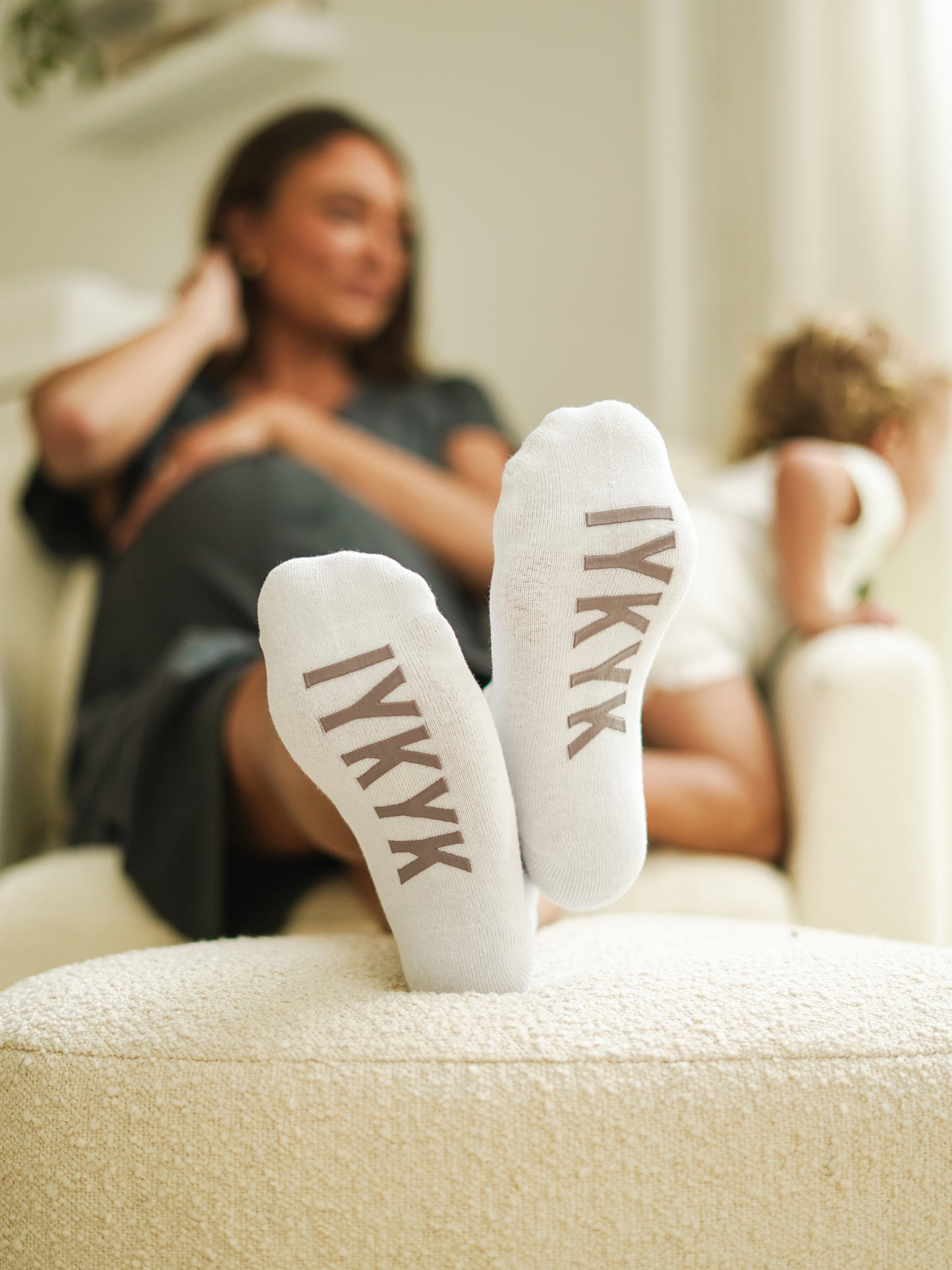 Model wearing IYKYK Labor & Delivery Socks sitting on chair with feet up on ottoman