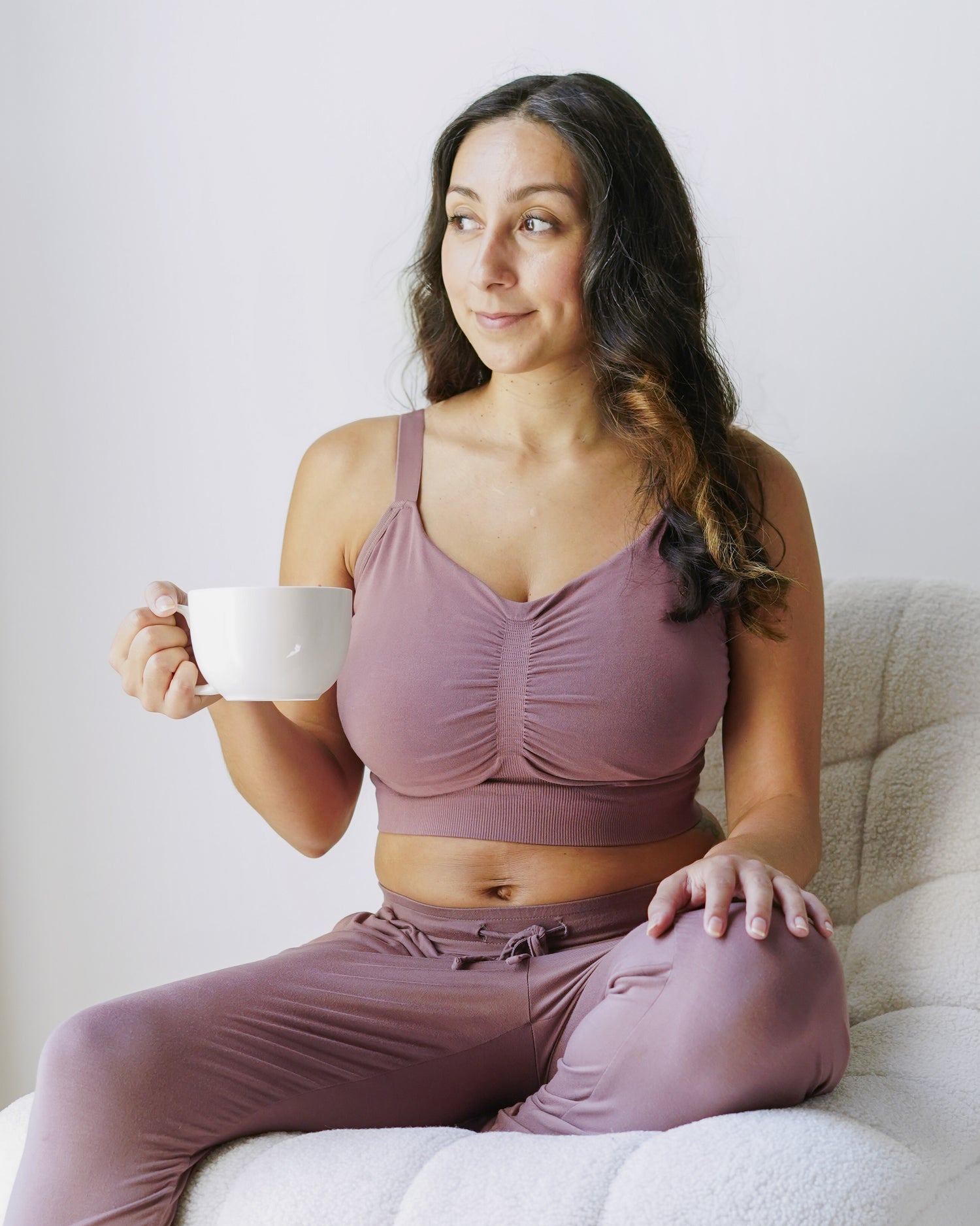Model sitting in chair holding mug wearing the Sublime® Bamboo Hands-Free Pumping Lounge & Sleep Bra in Twilight @model_info:Daniella is wearing a Small Super Busty.