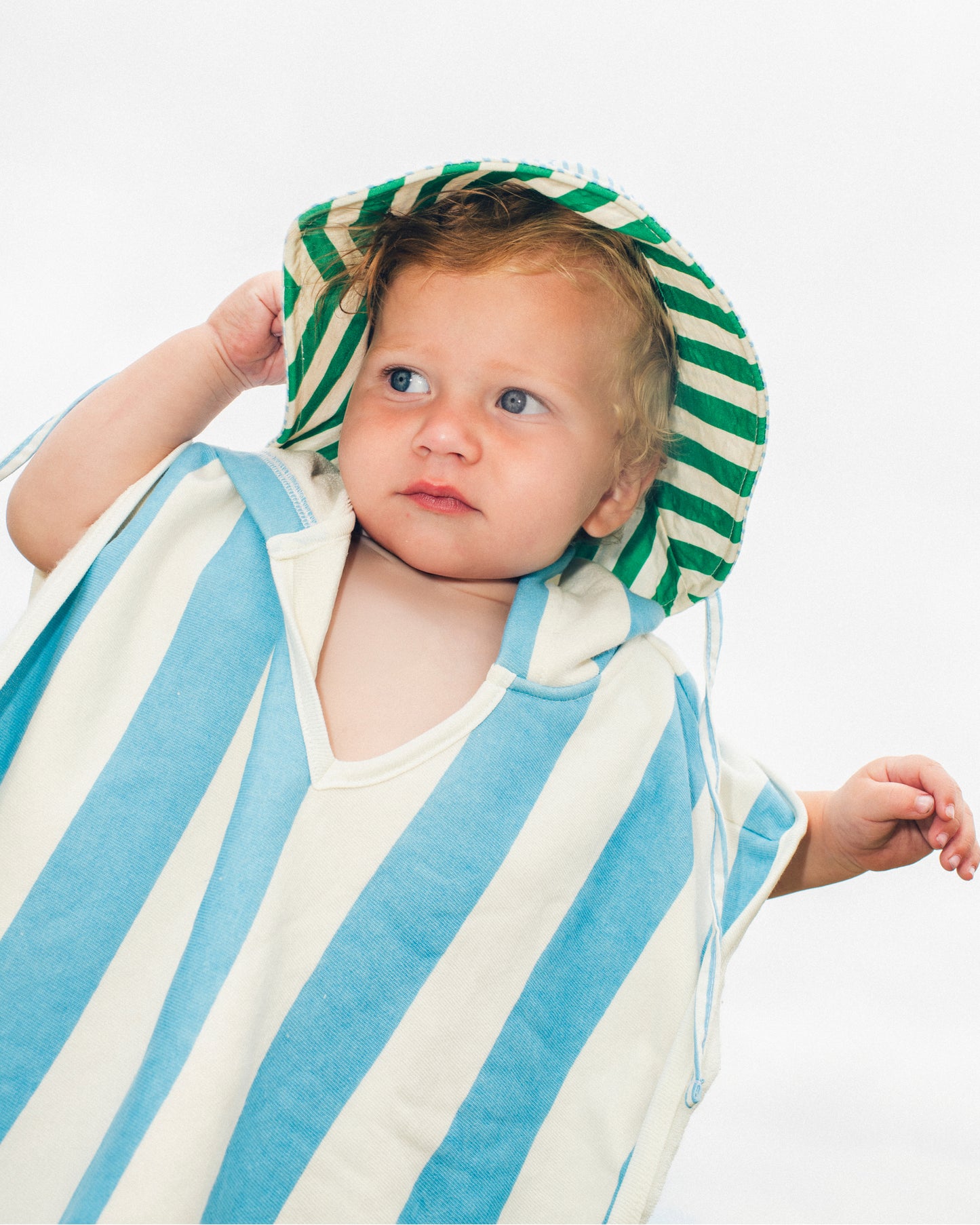 Image of toddler wearing the Organic Cotton Toddler Poncho Towel in Blue Wide Stripe and Big Floppy Sun Hat in Blue Pinstripe on a white background.