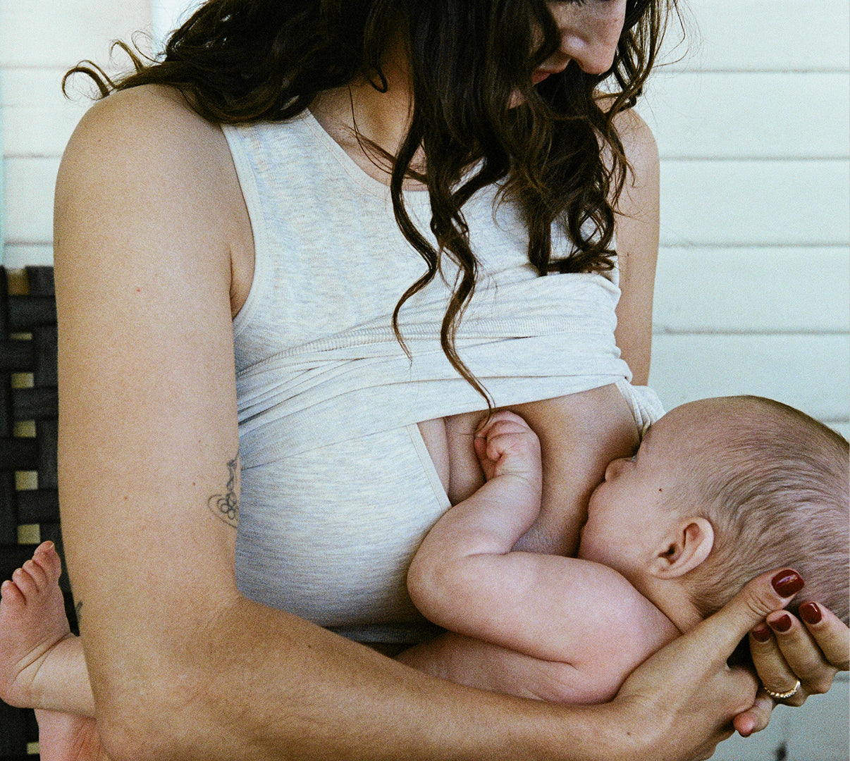 Woman breastfeeding baby on front porch while wearing Sublime® Bamboo Scoop Neck Maternity & Nursing Longline Bra Top in Oatmeal Heather showing how the outside fabric layer pulls up for nursing