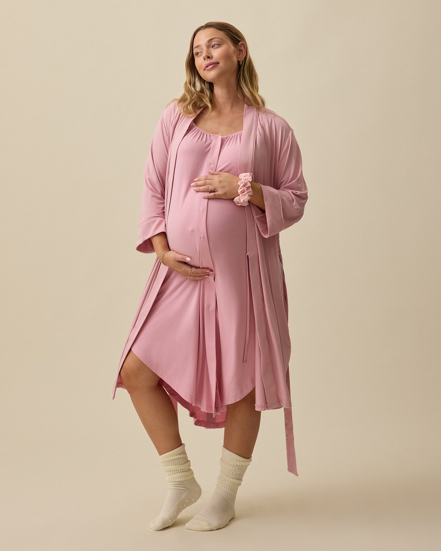 Model wearing Clea Robe in Light Mauve and Ruffle Strap Labor & Delivery Gown and Scrunchie in Light Mauve on a beige background.