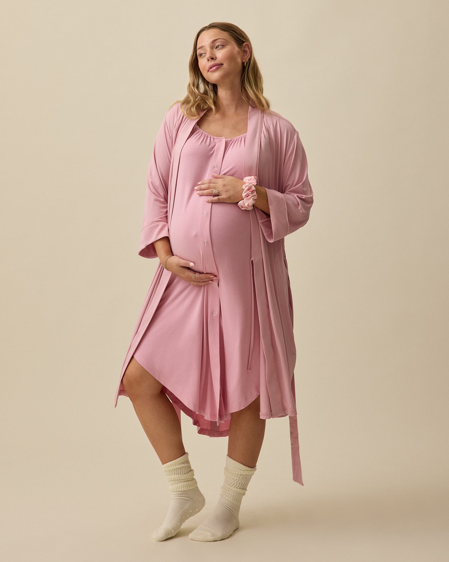Model wearing Clea Robe in Light Mauve and Ruffle Strap Labor & Delivery Gown and Scrunchie in Light Mauve on a beige background.