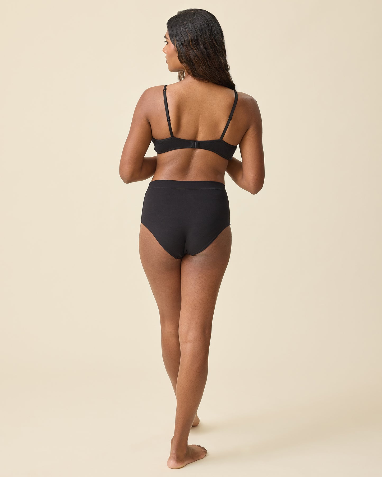 Back view of model wearing Every Stage Triangle Bralette in Black and Every Stage Brief in Black on a beige background.