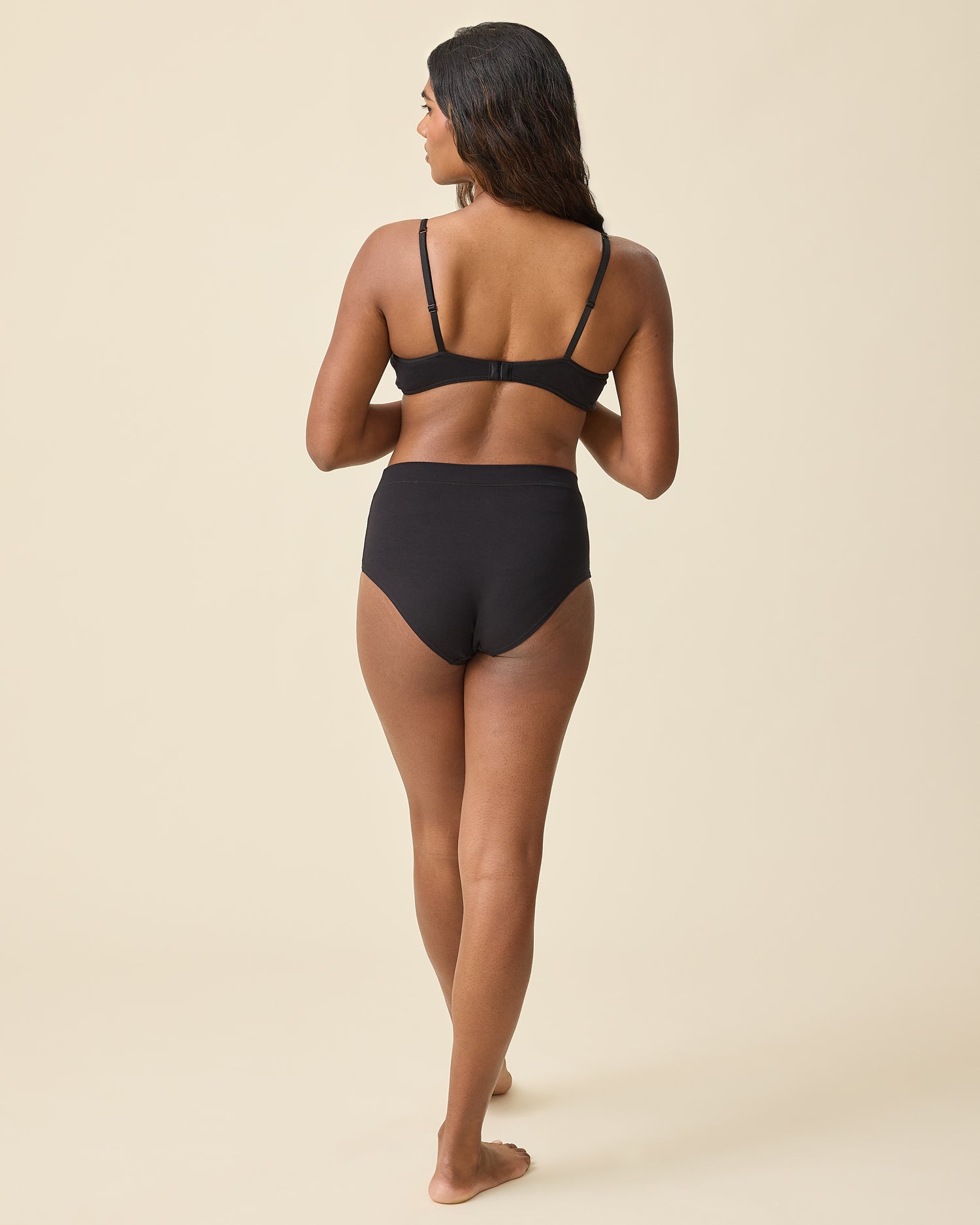Back view of model wearing Every Stage Triangle Bralette in Black and Every Stage Brief in Black on a beige background.
