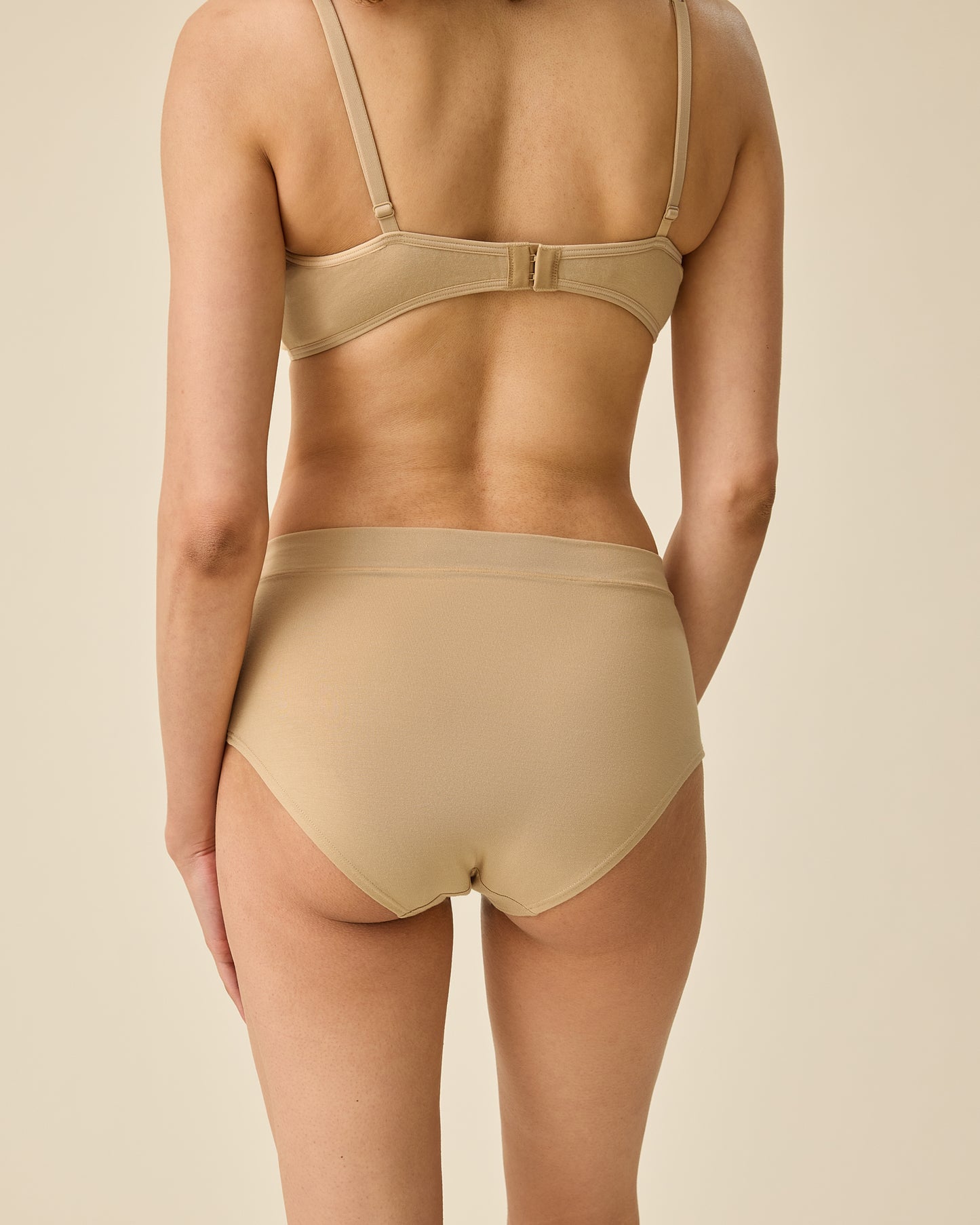Back view of model wearing Every Stage Brief in Toffee and matching bra on a beige background
