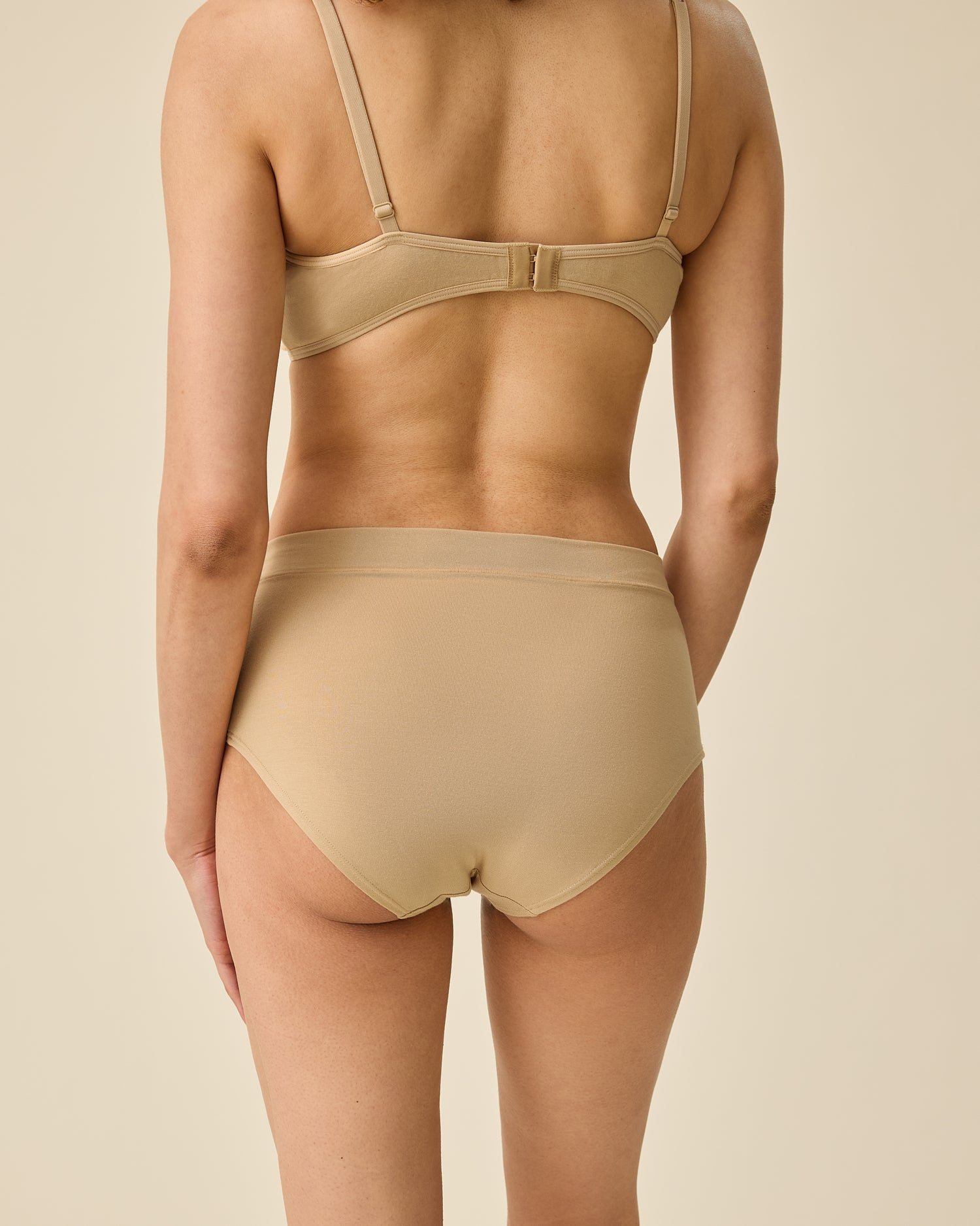 Back view of model wearing Every Stage Brief in Toffee and matching bra on a beige background