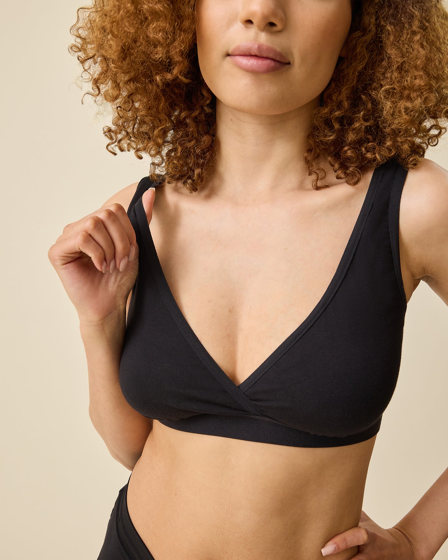 Model demonstrating nursing access on the Every Stage Crossover Bra in Black on a beige background @model_info: Devyn is wearing a Small.