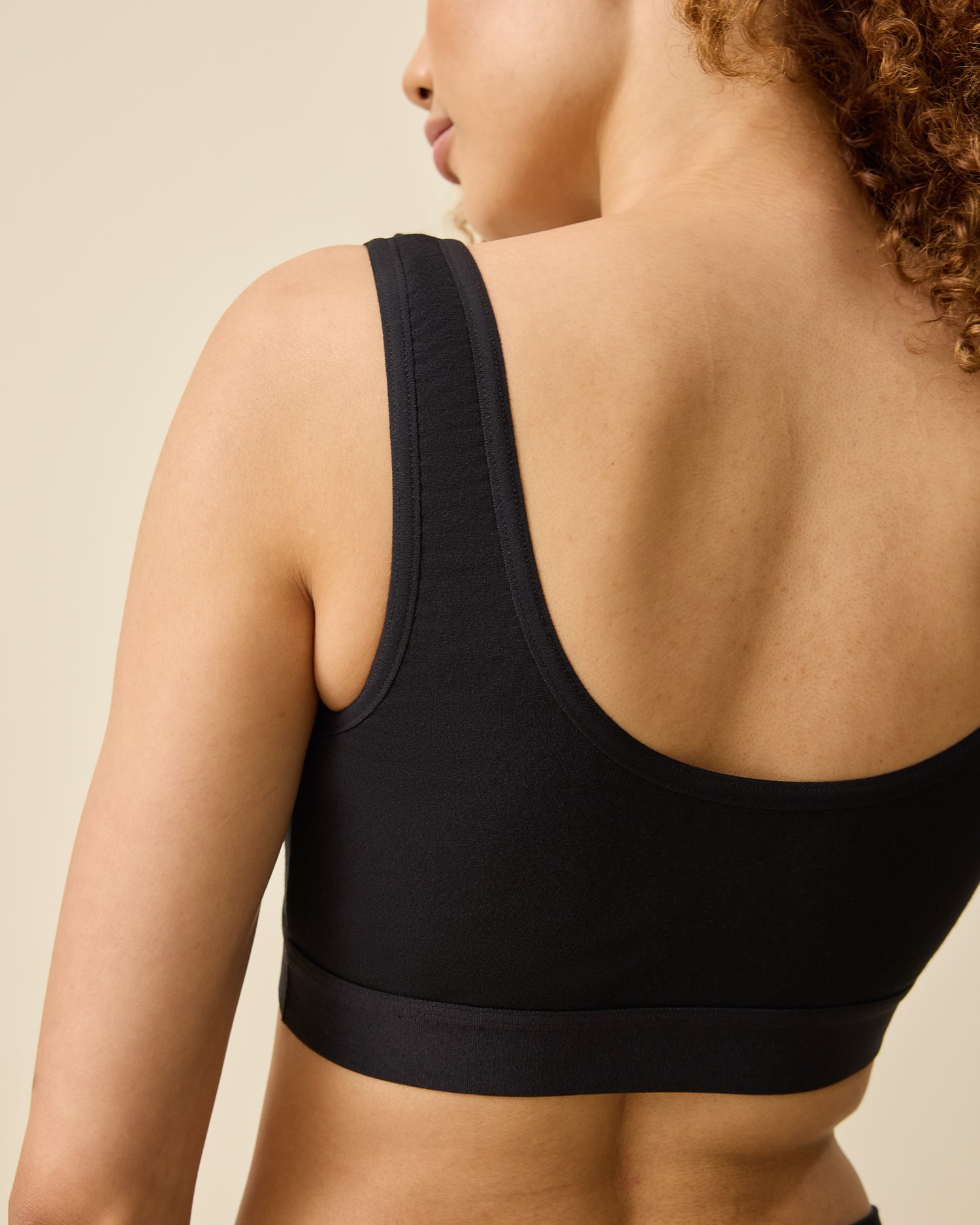 Back view of model wearing Every Stage Crossover Bra in Black on a beige background
