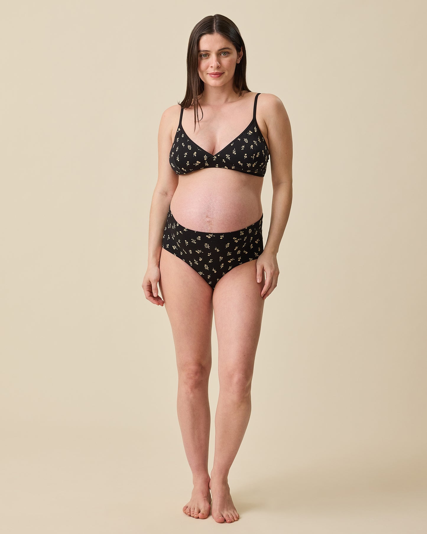 Pregnant model wearing Every Stage Brief and Triangle Bralette in Black Wildflower on a beige background