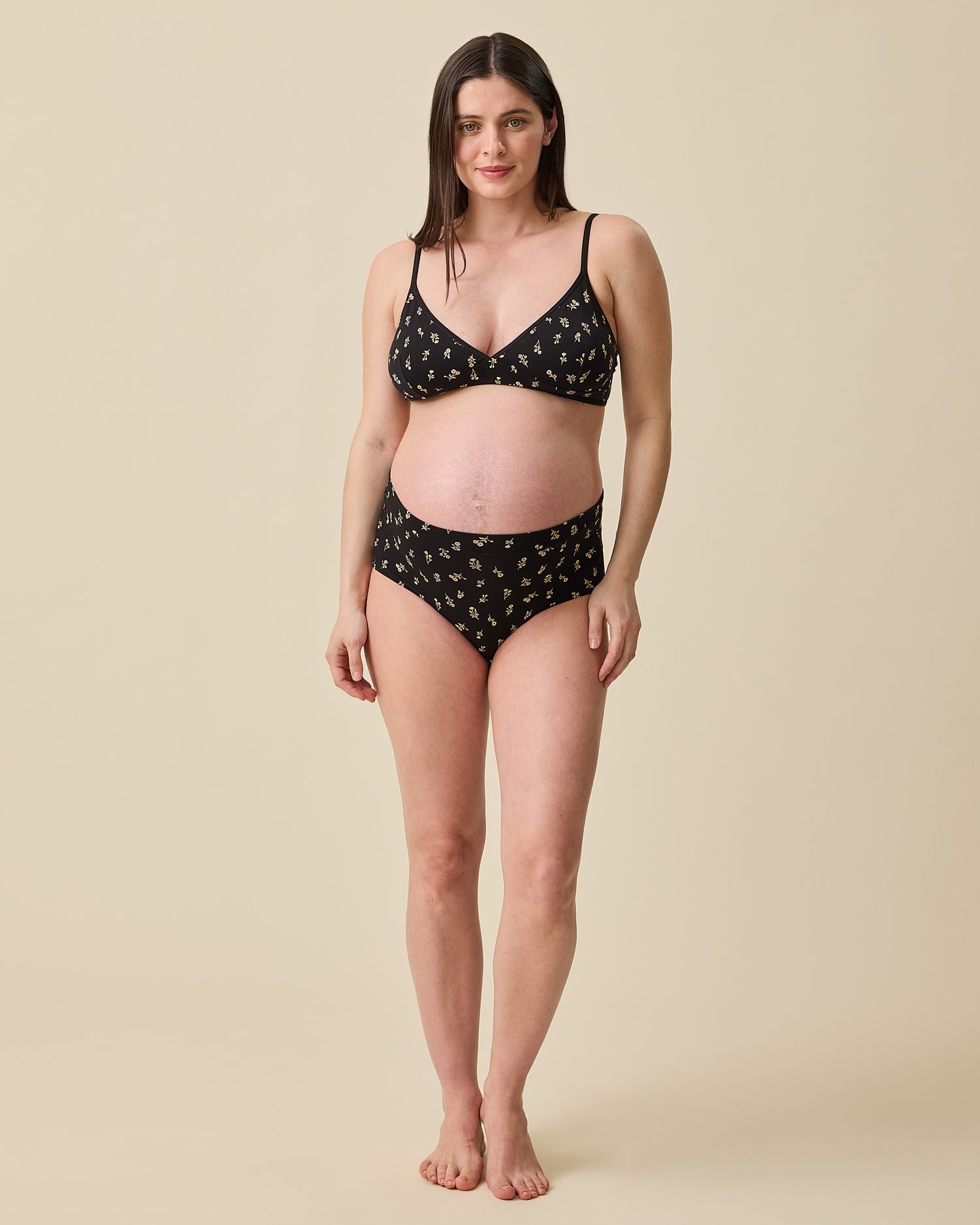 Pregnant model wearing Every Stage Brief and Triangle Bralette in Black Wildflower on a beige background