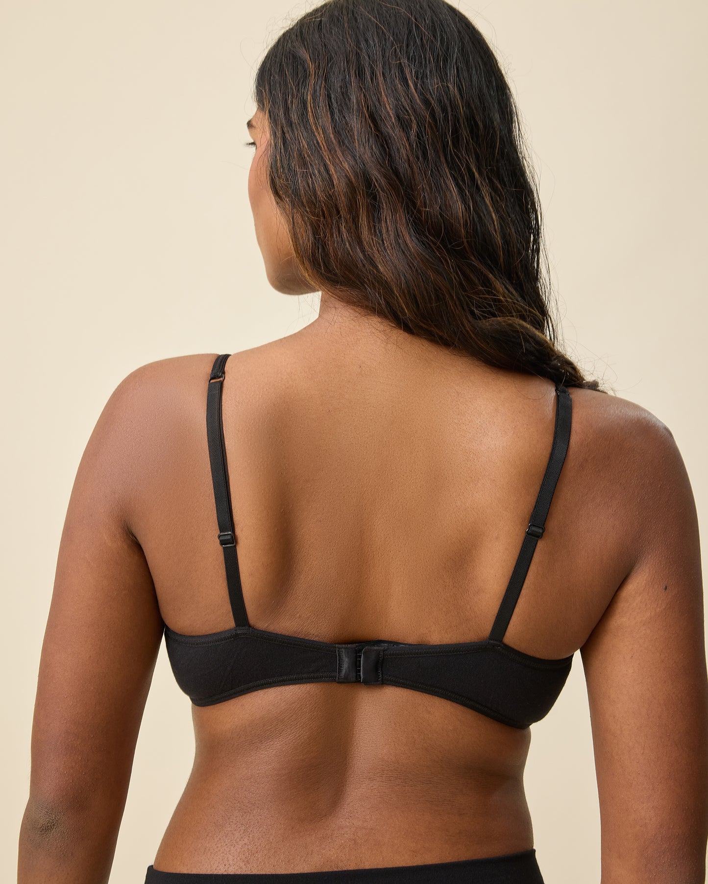 Back view of model wearing Every Stage Triangle Bralette in Black on a beige background