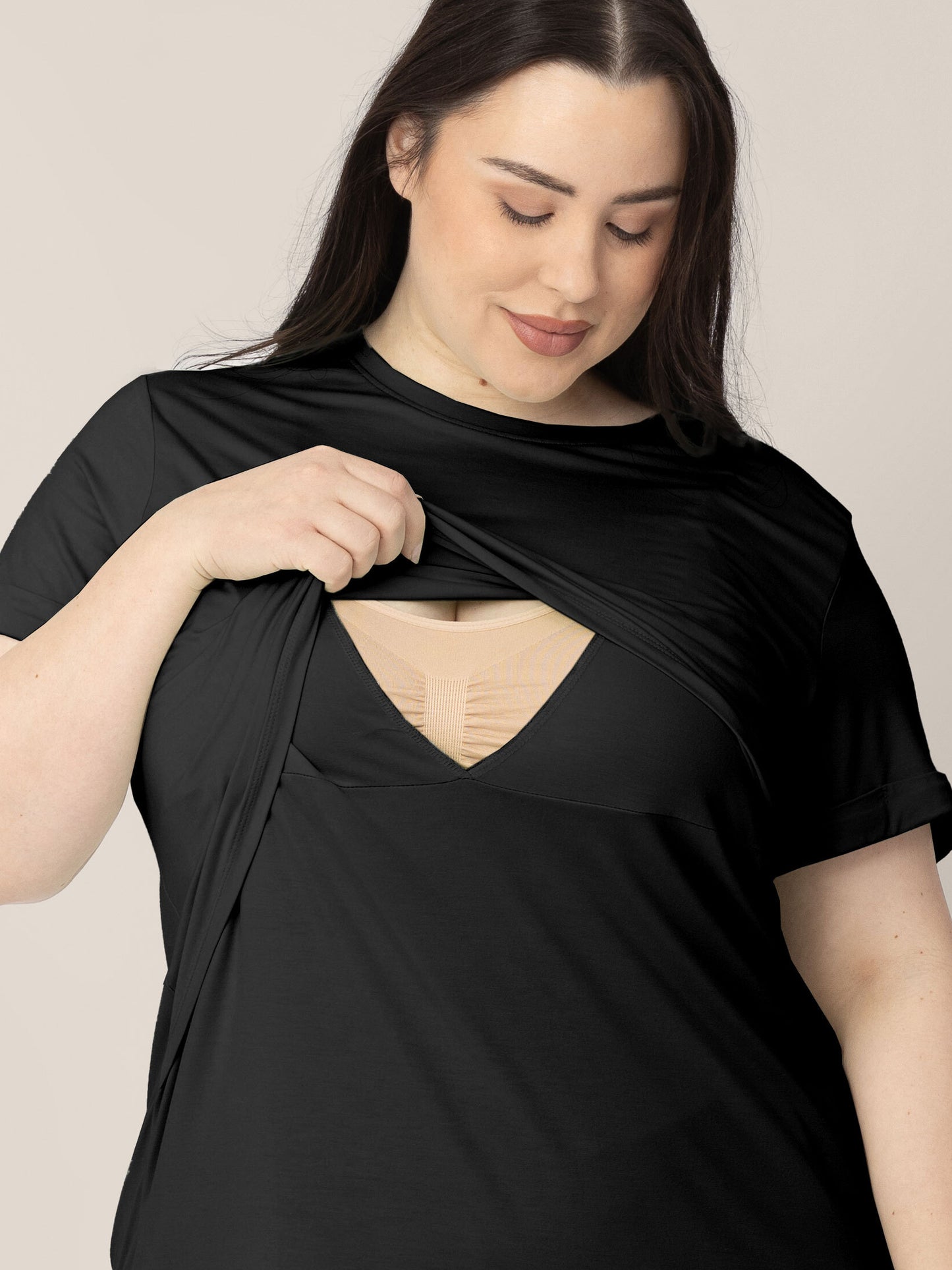 A model wearing the Everyday Asymmetrical Nursing T-shirt in Black, lifting the pull aside nursing flap to demonstrate the easy breastfeeding access.