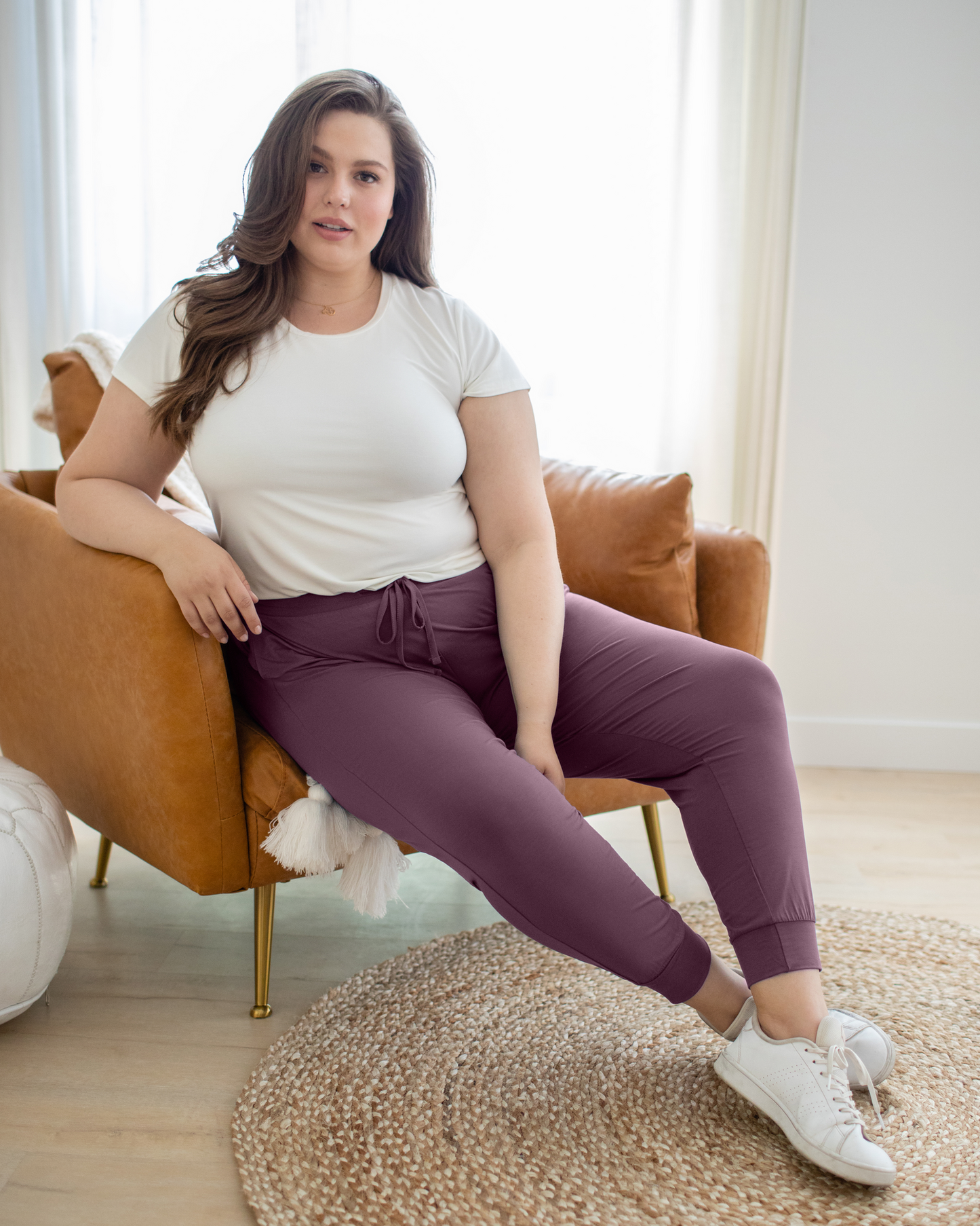 Model sitting in chair wearing the Everyday Lounge Jogger in Burgundy Plum, paired with Everyday Maternity & Nursing T-shirt in White and white tennis shoes