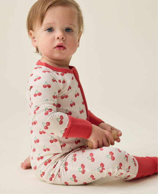 Baby wearing the Bamboo Baby Pajama with cherry pattern sitting on a beige background@model_info:Noa is wearing 6-12 months.