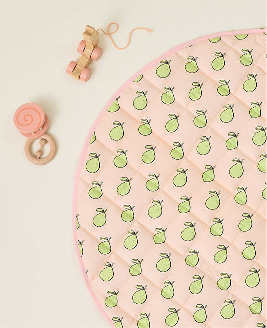 Round pink play mat with green pomelo pattern and some baby toys on a beige background