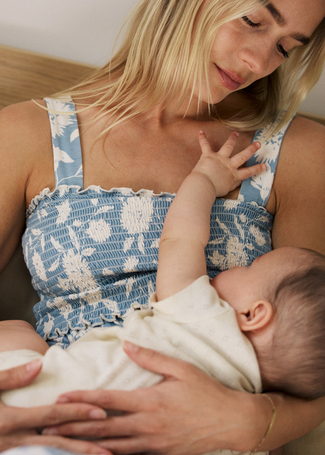 Woman wearing the Sienna Smocked Maternity & Nursing Dress in vintage blue floral pattern and nursing baby