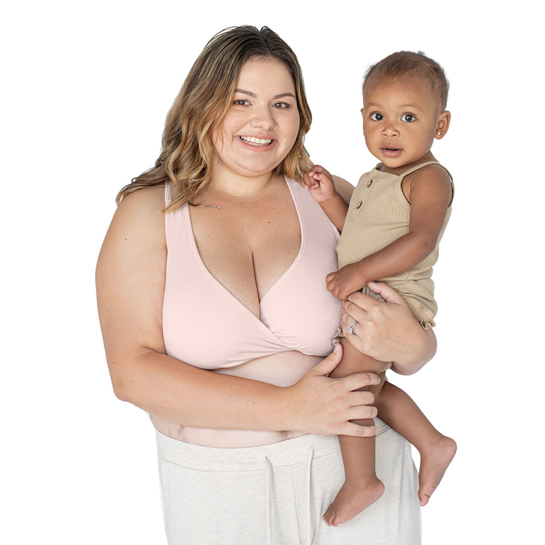 Model wearing the French Terry Racerback Nursing & Sleep Bra in Soft Pink holding her baby on her hip. 