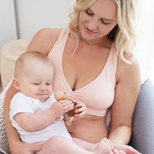 Model wearing the French Terry Racerback Nursing & Sleep Bra in Soft Pink with her baby on her lap. @model_info:Maddy is wearing a Small.