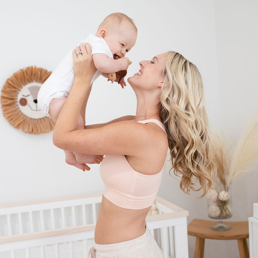 Model holding her baby up in the air wearing the French Terry Racerback Nursing & Sleep Bra in Soft Pink