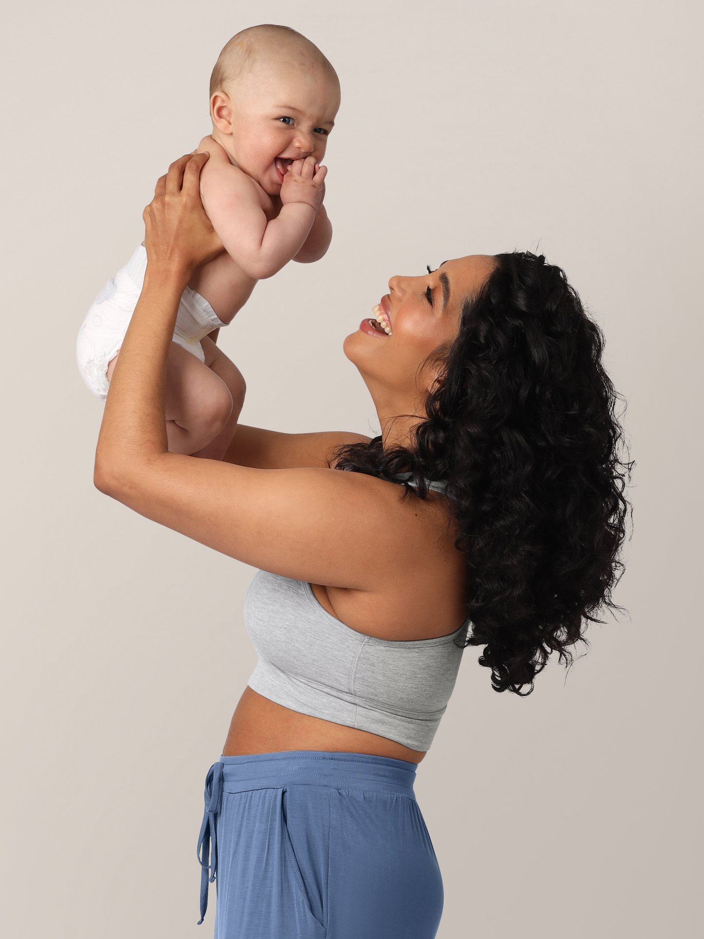 Side view of model wearing the French Terry Racerback Nursing & Sleep Bra in grey heather, holding baby above her