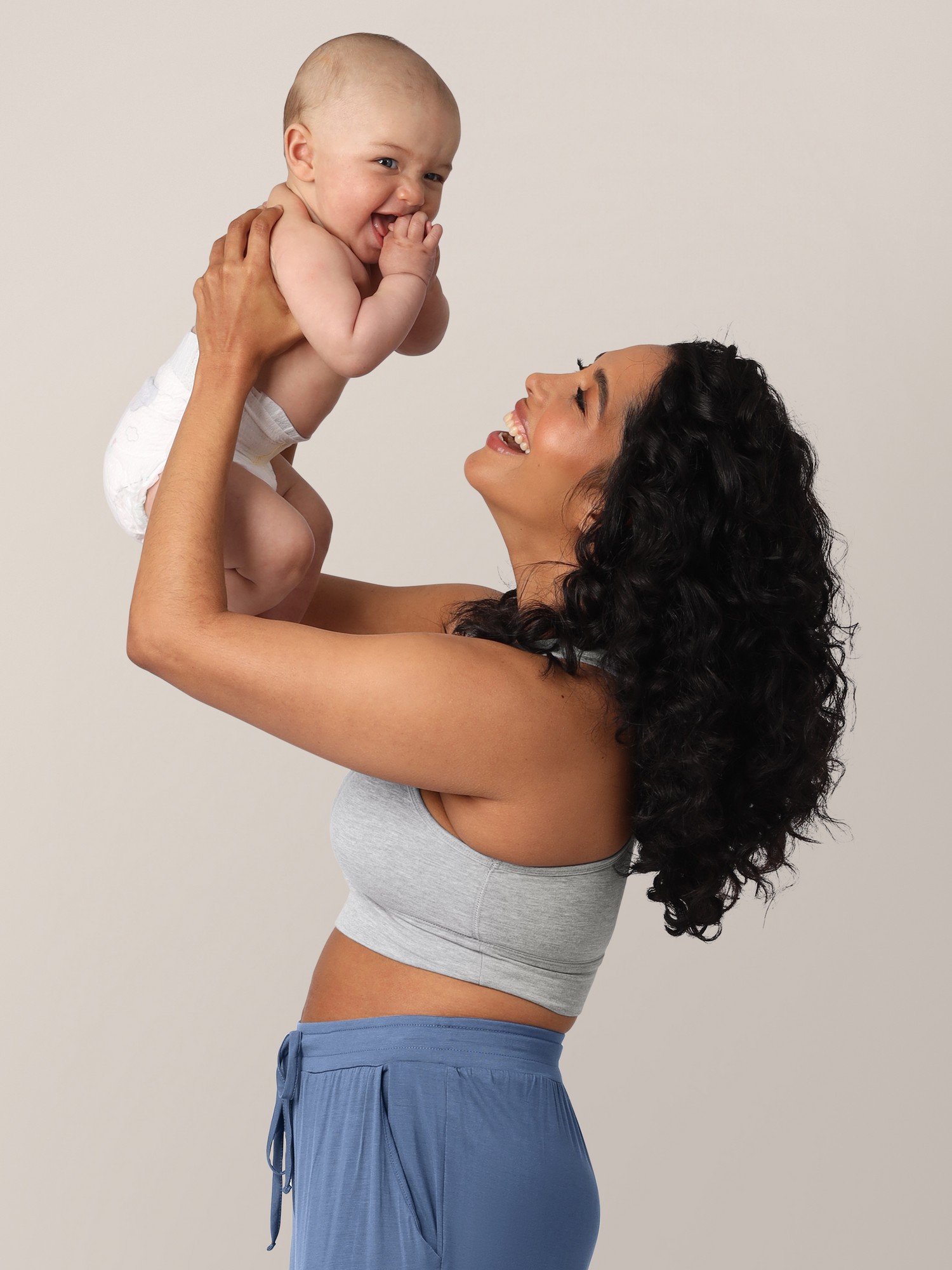 Side view of model wearing the French Terry Racerback Nursing & Sleep Bra in grey heather, holding baby above her