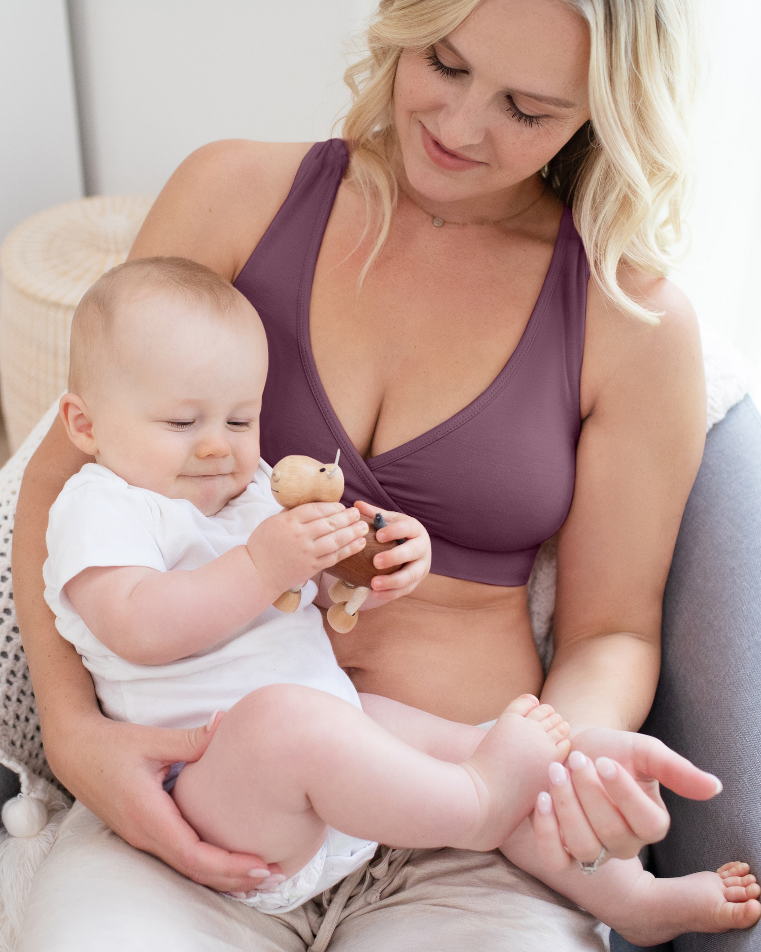 Front view of model sitting in chair with baby in lap, and wearing the French Terry Racerback Nursing & Sleep Bra in Burgundy Plum