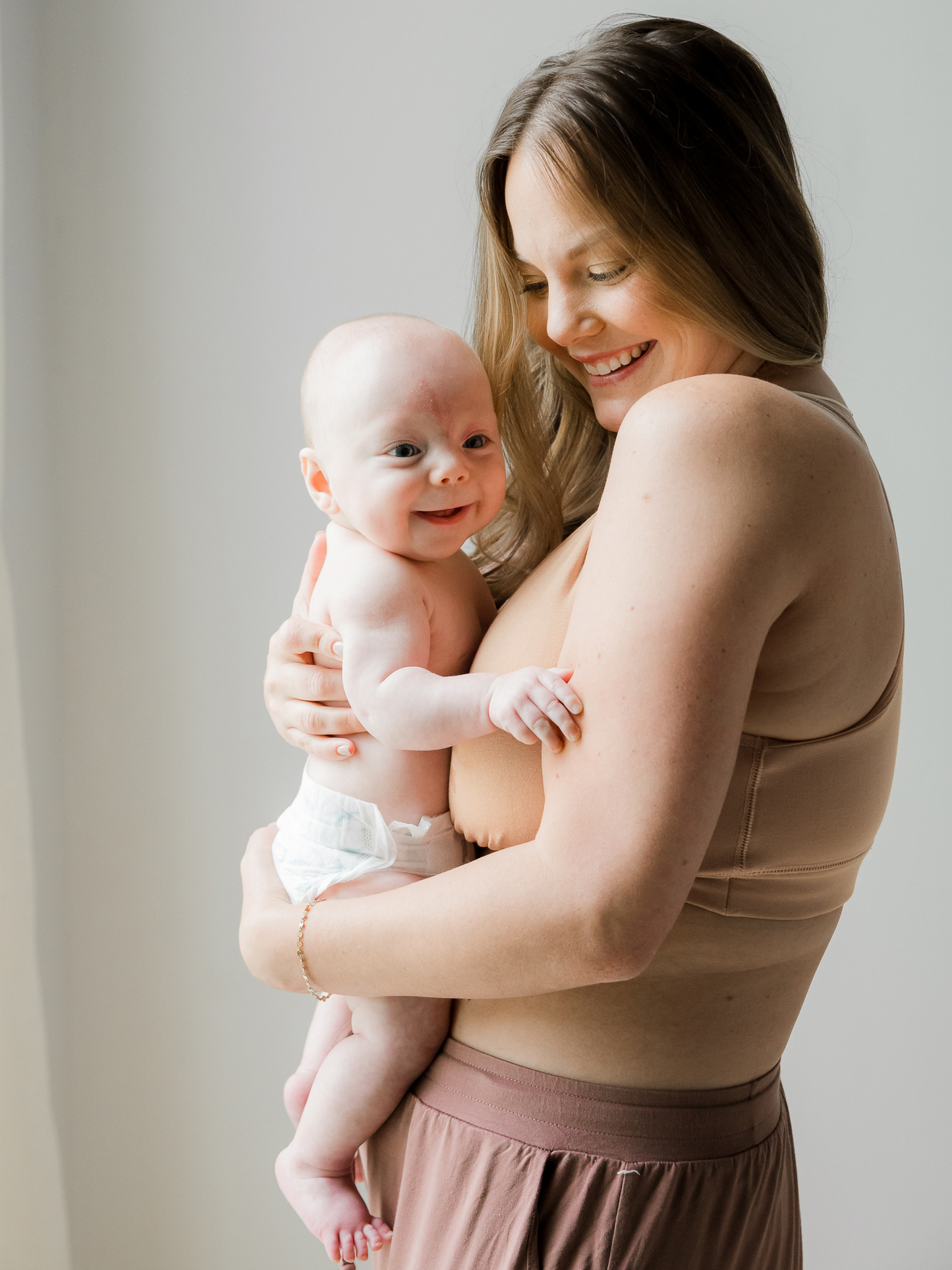 Side view of model wearing the French Terry Racerback Nursing & Sleep Bra in Beige and holding her baby against her
