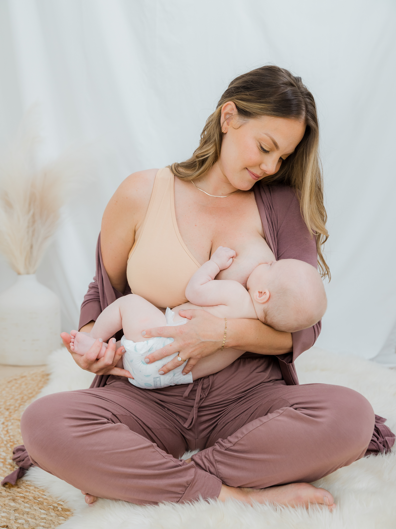 Model sitting and nursing baby, wearing the French Terry Racerback Nursing & Sleep Bra in Beige. @model_info:Ali is wearing a Large Busty.