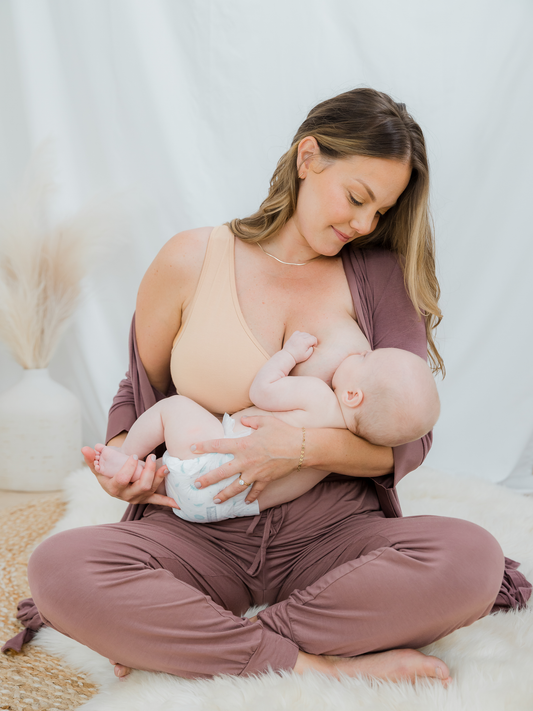 Model sitting and nursing baby, wearing the French Terry Racerback Nursing & Sleep Bra in Beige. @model_info:Ali is wearing a Large Busty.