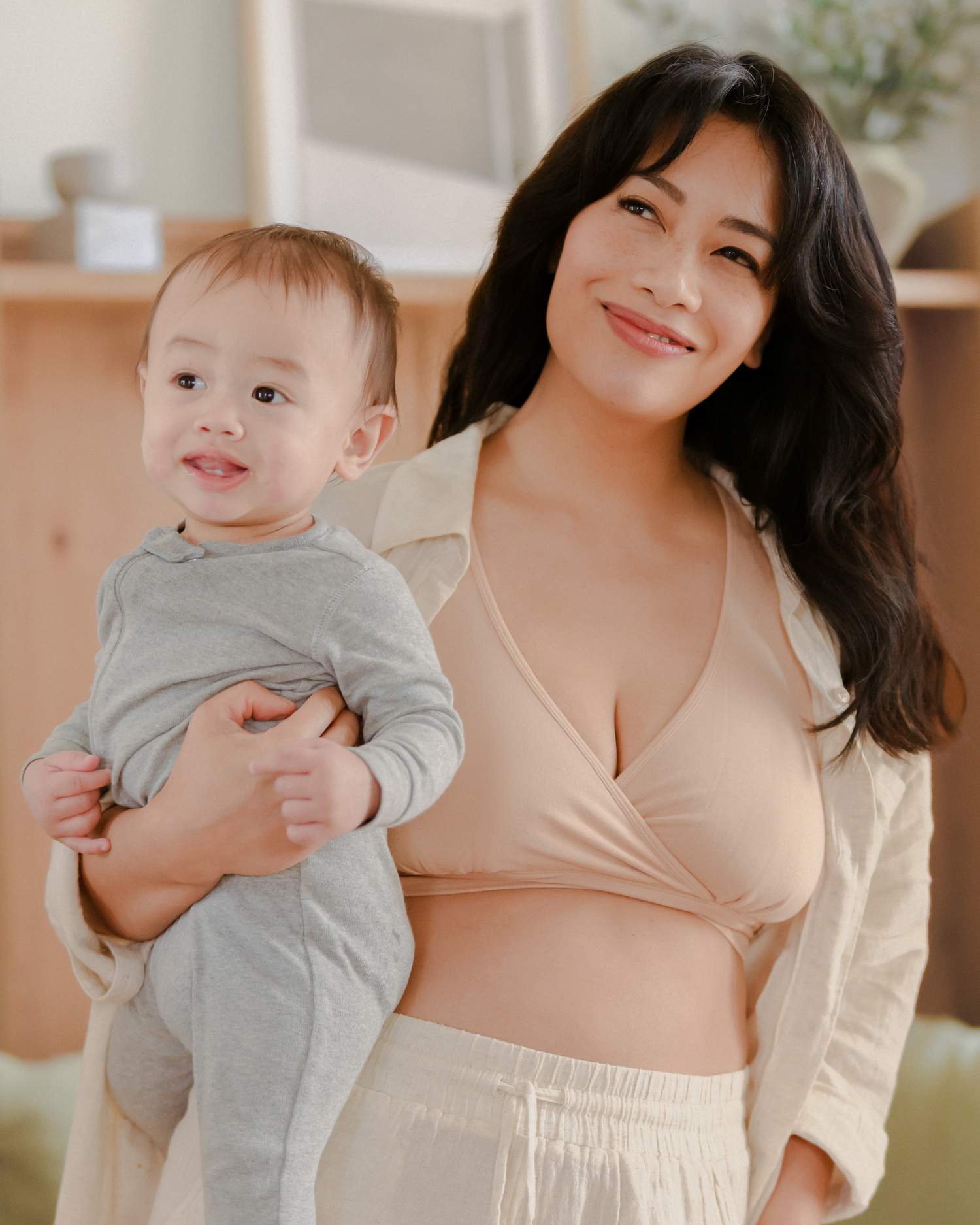 Model wearing the French Terry Racerback Nursing & Sleep Bra in Beige and holding her baby against her @model_info:Nikki is wearing a Medium.