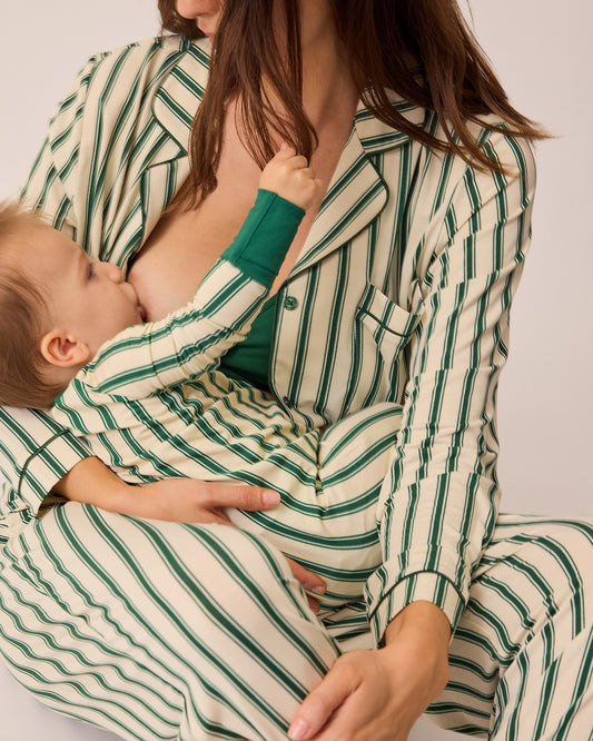 Model is holding baby in matching long sleeve onesie and breastfeeding while sitting on floor and wearing Clea Bamboo Long Sleeve Pajama Set in Green Candy Stripe, on a beige background.