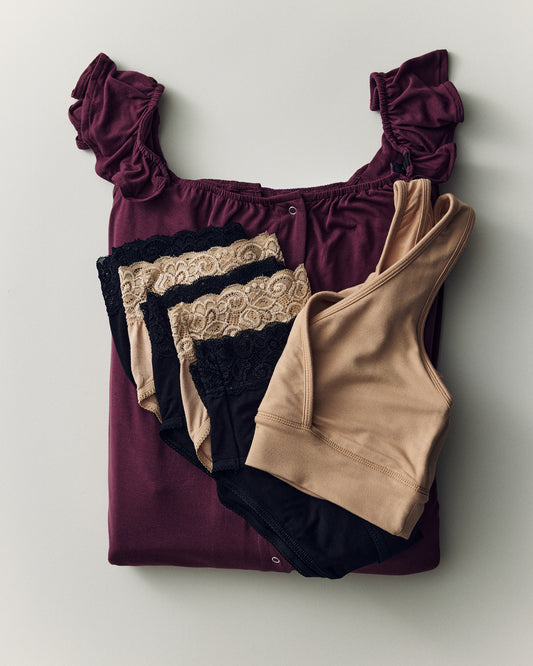 Flat lay of Ruffle Gown Labor & Delivery Bundle, displaying a folded Gown, five undies, French Terry Racerback Nursing & Sleep Bra, on a beige background. Not seen is Robe, also included.