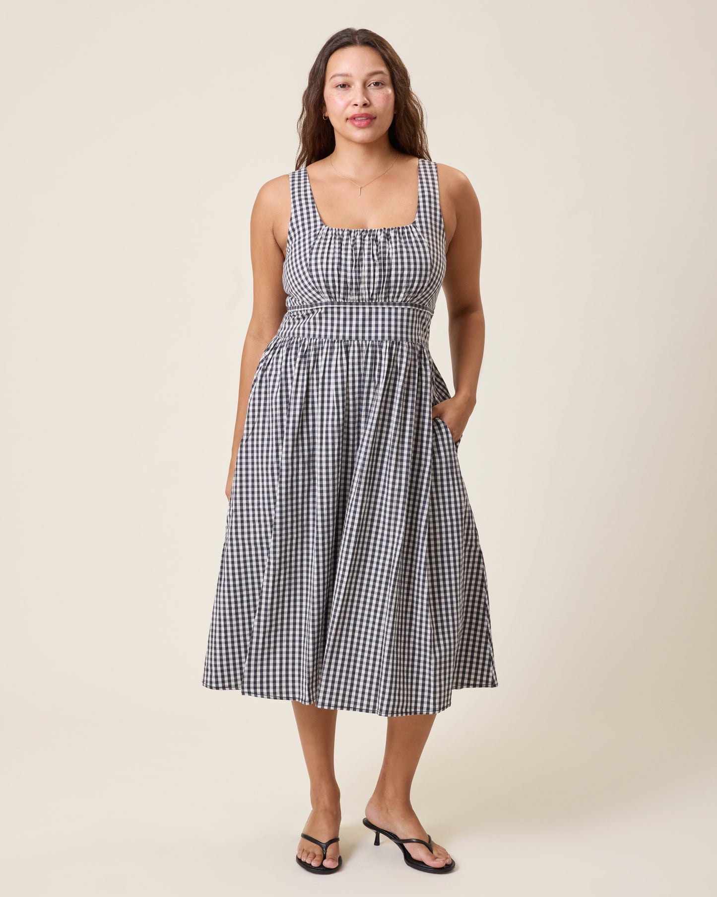 Front view of model wearing Gracie Poplin Nursing Midi Dress in Black & White Gingham on a neutral background and with a hand placed in the dress's pocket@model_info:Alana is 5'7" and wearing a Large.
