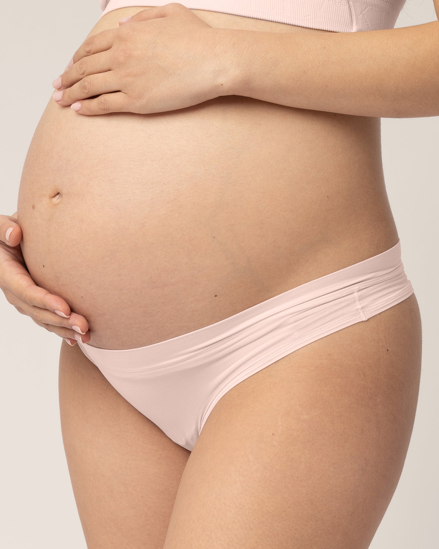 Close up of model who is pregnant and wearing Grow with Me™ Maternity & Postpartum Thong in Soft Pink on a beige background.