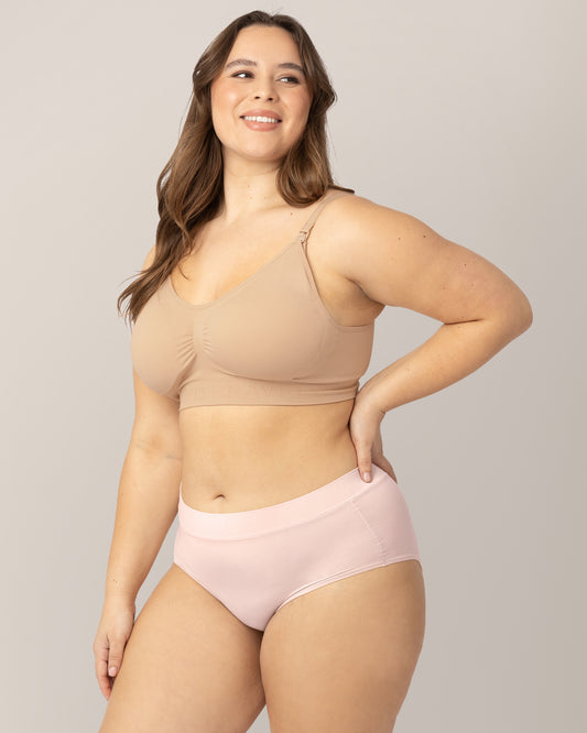 Model wearing the Grow with Me™ Maternity & Postpartum Brief in soft pink with her hands near her stomach. @model_info:Venezia is wearing a Large.