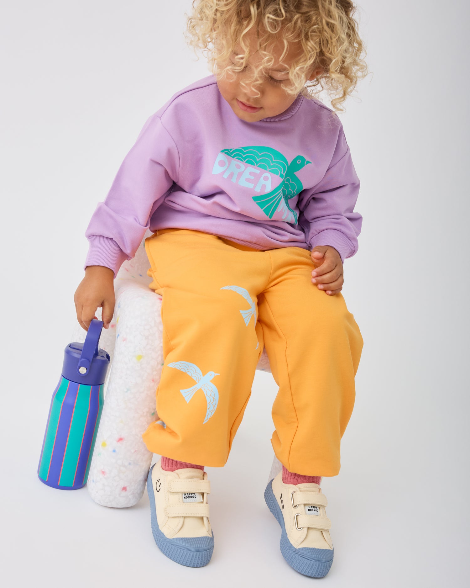 Child is sitting on chair and holding the handle of the Cool Kid Water Bottle in Navy & Green Stripe.