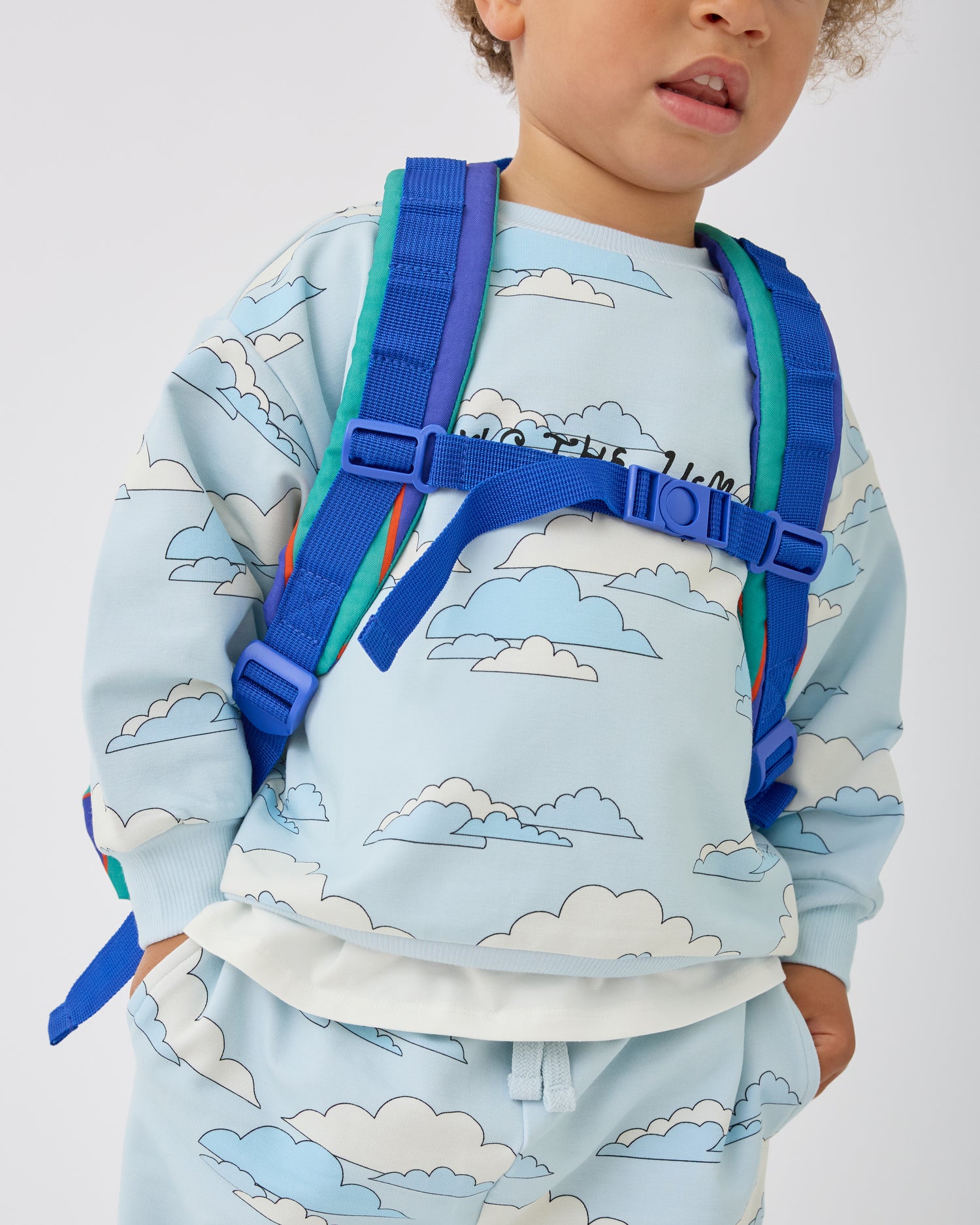 Close up of the shoulder straps and clip on the Cool Kid Backpack in Navy & Green Stripe on a beige background.