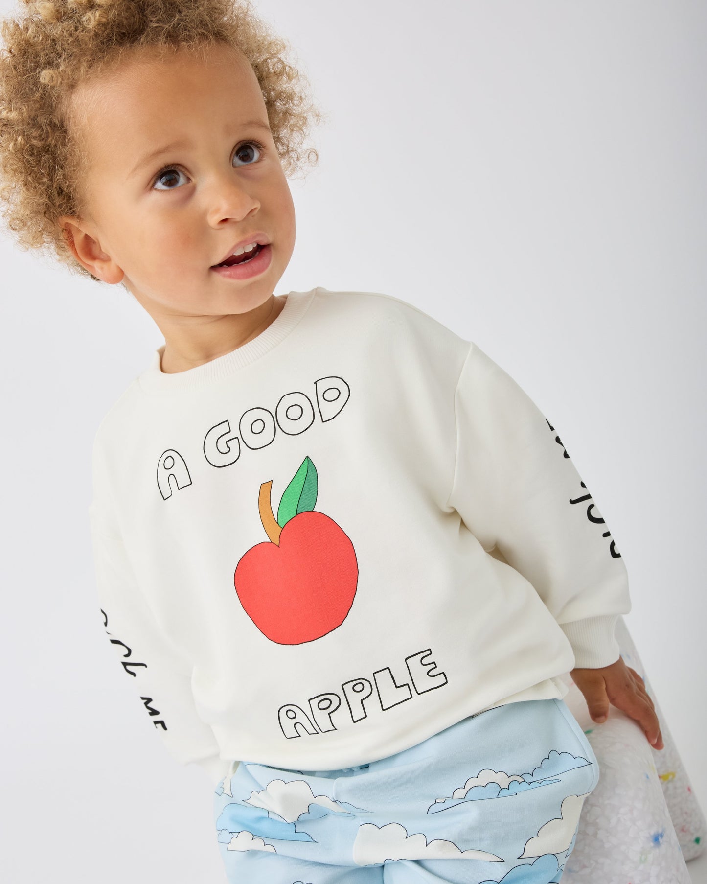 Model is wearing French Terry Jogger in Blue Clouds and Graphic Sweatshirt in Ivory Apple on a gray background.@model_info:Giles is 2 years old and wearing 4T.