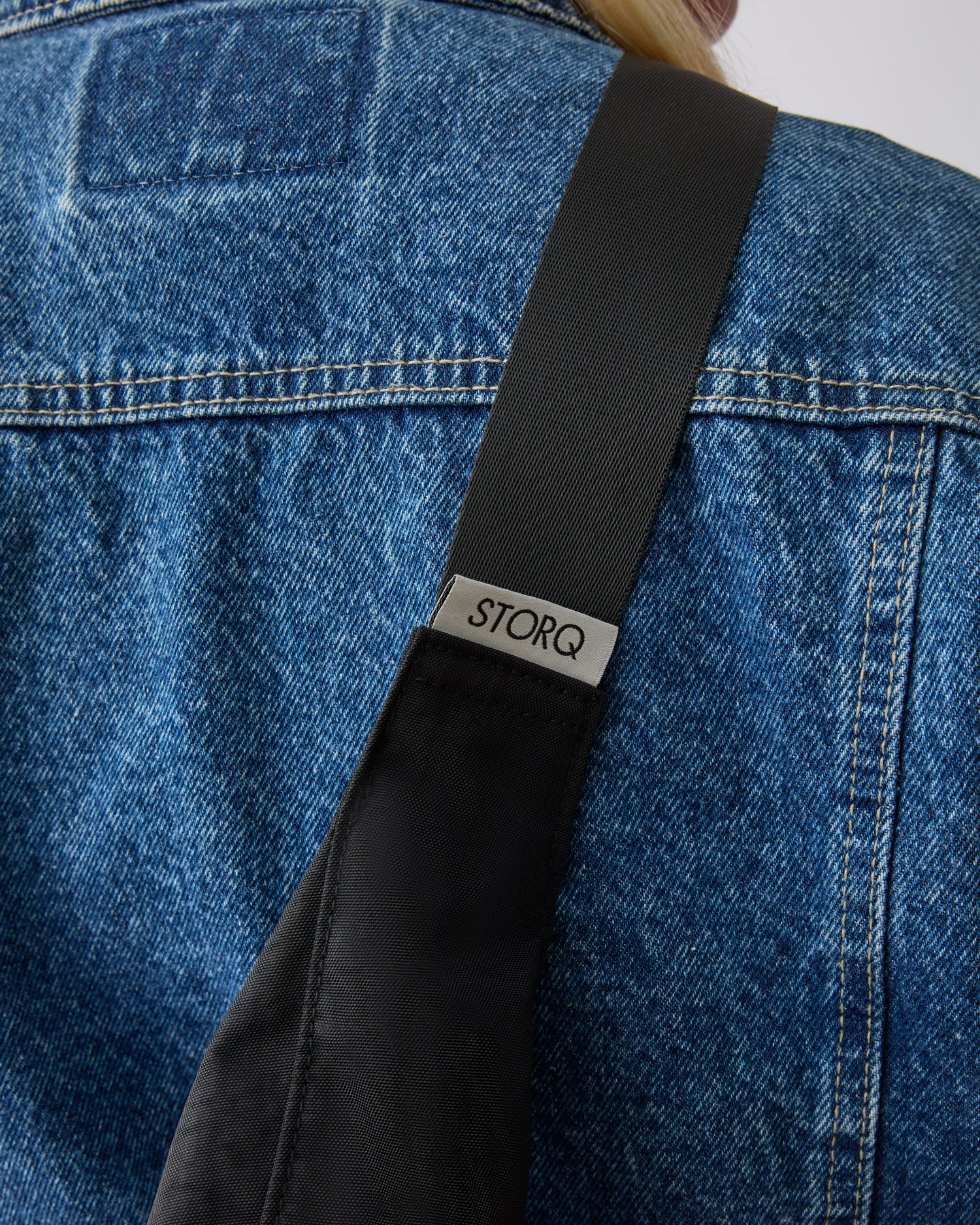Close up of the model wearing Half Moon Crossbody Bag in Black over shoulder and across the back, on a beige background.
