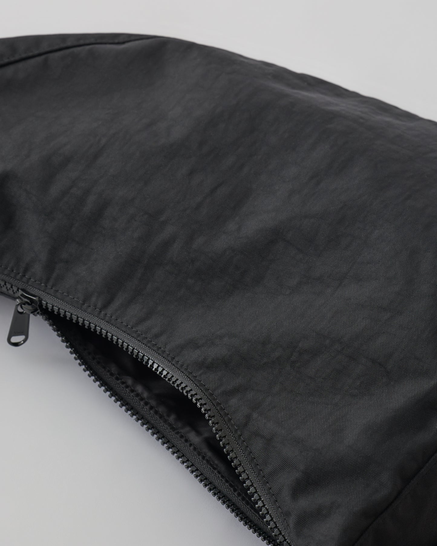 Close up of zipper on Half Moon Crossbody Bag in Black on a beige background. 