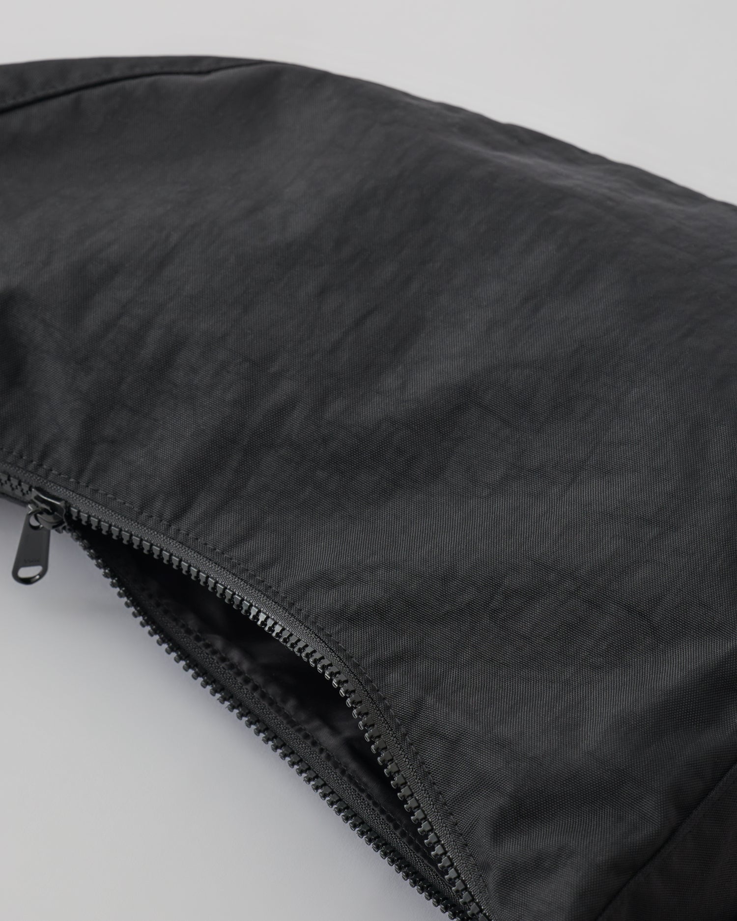 Close up of zipper on Half Moon Crossbody Bag in Black on a beige background. 